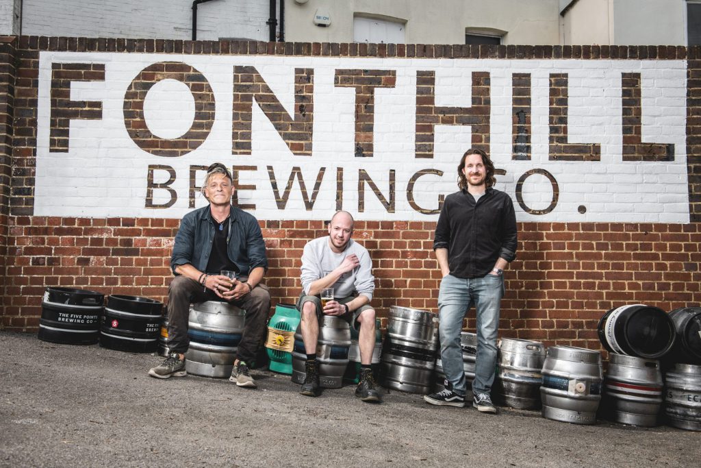 The Fonthill Brewing Co. team sitting in front of their logo, stencilled on to a brick wall outside the brewery