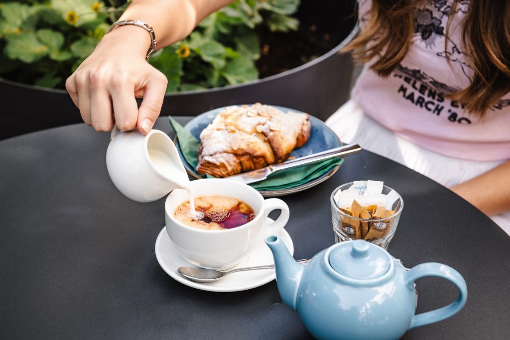 Fresh milk pouring into a cup of tea next to a tea pot and almond pastry at the Philanthropist cafe and bar in Tunbridge Wells